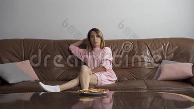 无聊的年轻女人坐在棕色的皮革沙发上看电视。 家庭主妇用遥控器<strong>切换</strong>频道