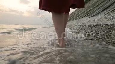 近景后景的双腿白种人女孩走在海边的石头海岸的水中，走向夕阳。