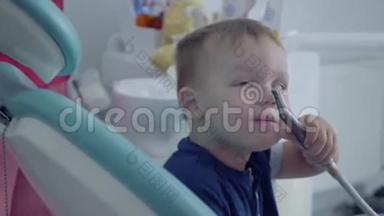 爱的牙医用双手检查坐在椅子上的无忧无虑的小男孩的牙齿，给他看一张镜子特写