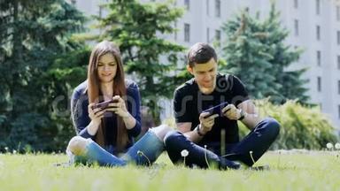 幸福夫妇在智能手机上玩手机游戏，坐在公园的草地上。 男人赢了比赛，女人输了。