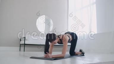 穿着运动服的一个苗条的黑发女人站在地毯上的四个人身上，正把腿往后抬。