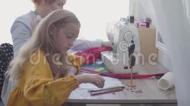 小女孩坐在前台的桌子旁，红发的妈妈在旁边缝衣服