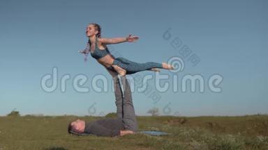 一对夫妇在草地上做杂技表演，身穿运动服的年轻白种人正在平衡她的男伴的腿