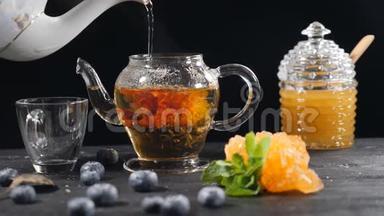 在玻璃茶壶里倒开水。 绿色的中国花茶绽放。 红花茶的漂浮。 蓝莓