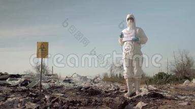 环保主义，穿着防护服装的妇女，戴着面具，在垃圾填埋场张贴有防止污染标语的海报