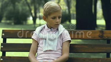 不快乐的小男孩独自坐在公园的长凳上，<strong>校园欺凌</strong>和残忍