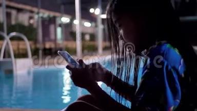 晚上在<strong>游泳</strong>池附近使用智能手机放松的<strong>儿童</strong>女孩。