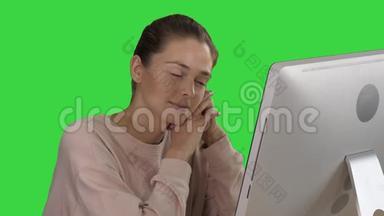 金发女孩带着粉红色的套头衫，看着显示器上的电脑在绿色屏幕上观看视频，色度键。
