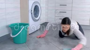 幸福的女人戴着粉红色的橡胶手<strong>套用</strong>一块布洗厨房的地板。 地板上的灰色瓷砖。