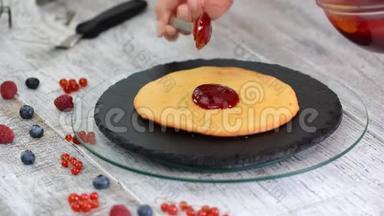 女人把浆果酱放在蛋糕层上。 在白色背景下在蛋糕上做分层蛋糕。
