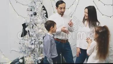 父母和两个兄弟姐妹<strong>聚集</strong>在圣诞树附近，互相转告他们的新年愿望，弯曲的手指。