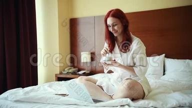 一个姜黄色的微笑女人坐在酒店房间的床上喝着茶
