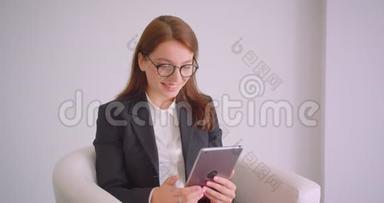戴着眼镜的年轻白种人女商人的特写肖像，她坐在扶手椅上<strong>观看</strong>平板电脑的<strong>视频</strong>