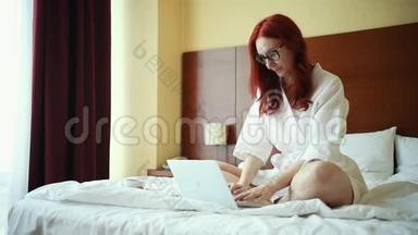一个<strong>姜黄色</strong>的微笑女人坐在酒店房间的床上，拿着笔记本电脑工作