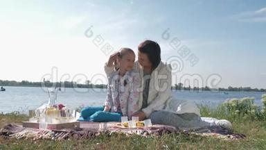 母爱，快乐的年轻妈妈在草地上的家庭野餐中与小女孩拥抱