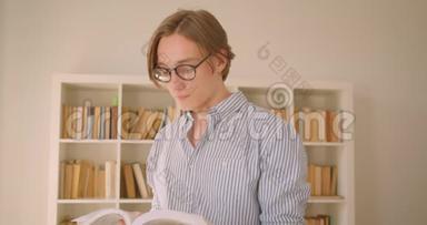 一位年轻成功的高加索男学生戴着眼镜看着<strong>图书馆</strong>里的照相机<strong>看书</strong>的特写肖像