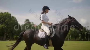 阳光明媚的一天，身穿白色西装，头戴黑色头盔的年轻美女骑着马在露天的竞技场上骑马