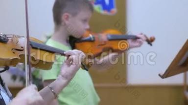 在音乐学校的音乐课上，小男孩学生和老师一起拉小提琴。