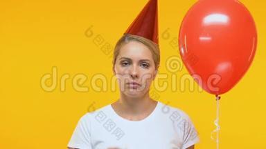 沮丧的女士戴着生日帽，拿着气球，吹着党的号角，孤独