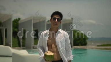 在阳光明媚的日子里，穿着无扣白色衬衫和太阳镜在室外游泳池散步的亚洲年轻人，异国情调的酒店