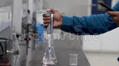 一位研究科学家用一个微型吸管将无色化学物质从锥形烧瓶中倒入烧杯的手