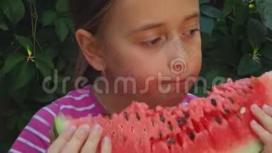 少女在绿色植物的背景下吃一个香甜多汁的西瓜。 孩子享受一大片西瓜..