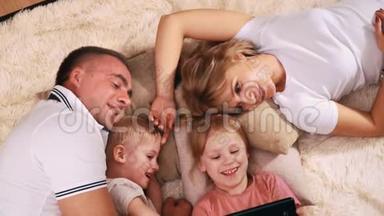 <strong>一家人</strong>躺在枕头上的毯子上，看着他们<strong>女儿</strong>拿着的平板电脑。
