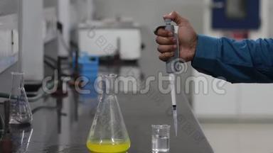 一位科学家的手把一种<strong>无色</strong>的化学物质从一个微型吸管倒入一个锥形的黄色化学物质