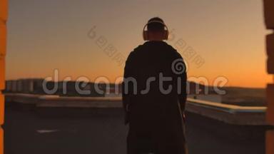 日落时分，一个人戴着耳机走在屋顶上，从日落时分摩天大楼的高度看着这座城市。 放松放松