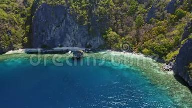 菲律宾船只漂浮在蓝色泻湖中，漂浮在巨大的悬崖岩石前的珊瑚礁顶部。 El Nido