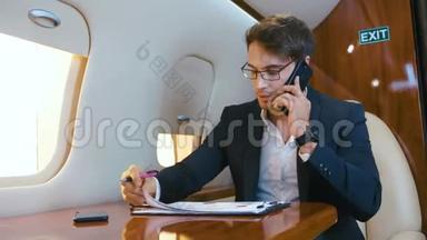 忙碌的商人在私人喷气式飞机上飞行时，处理文件和在手机上交谈。 飞机
