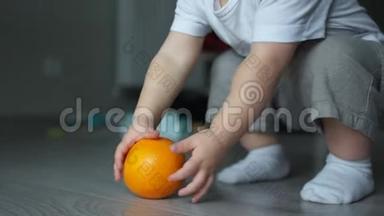 特写镜头，一个两岁的婴儿从地板上举起一个橘子.. 儿童和素食主义者，健康饮食