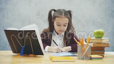 灰色背景<strong>的</strong>聪明女学生。 在这段时间里，他坐在桌子旁。 <strong>写作业</strong>。