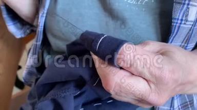 一位年长的老奶奶用针缝衣服，双手合拢