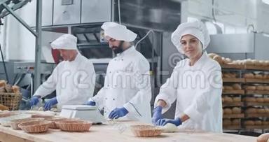 非常有魅力的面包师女人带着大大的微笑，她的同事则是面包师们在面团中烘烤面包