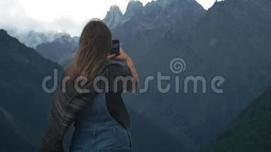 年轻迷人的女孩旅行者-博客<strong>制作</strong>了一张大山的照片在智能<strong>手机</strong>上。 穿着暖和的衣服