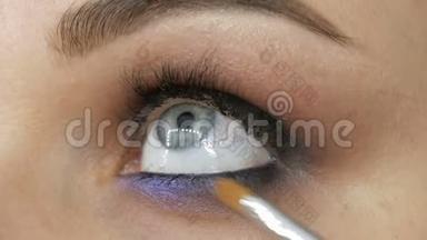 美丽的蓝眼睛是一个年轻的女人，她用特殊的刷子、丁香和珍珠般的烟熏眼睛涂着烟熏的眼睛