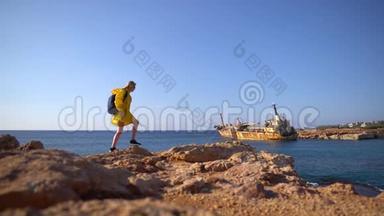 美丽的年轻女游客，穿着黄色雨衣，在风景如画的大海背景下走在岩石海滩上，老了