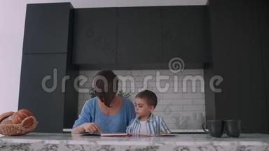 一位年轻的西班牙母亲和她的儿子坐在桌子旁，教他读孩子帮助和鼓励他的儿子，