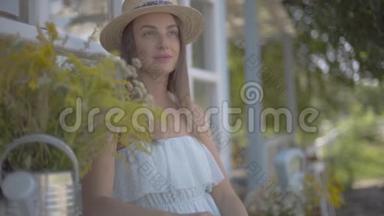 迷人的年轻女子戴着草帽和白色的连衣裙坐在小村房子前面。 <strong>农村生活</strong>方式。 慢慢