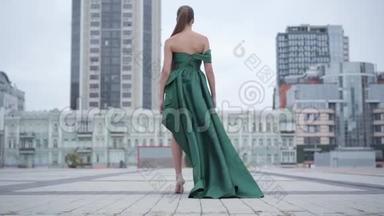 美丽美丽美丽的女孩，穿着一件漂亮的晚绿色连衣裙，迷人地走在附近空荡荡的城市广场上