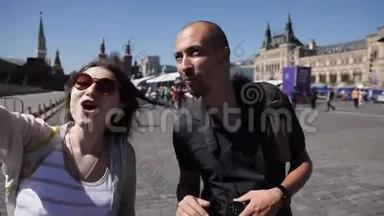 两个旅行者，一个男人和一个女人，在大都市的广场上走来走去，拍照。 女孩要求男人