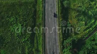 高空俯视图：深色汽车行驶在一条沥青路上，在阳光明媚的夏日穿过广阔的森林。