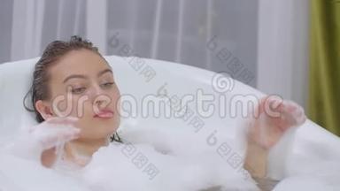 美丽的女人躺在浴缸里泡<strong>澡</strong>放松。 在有泡沫泡浴的浴缸里轻松愉快地躺着