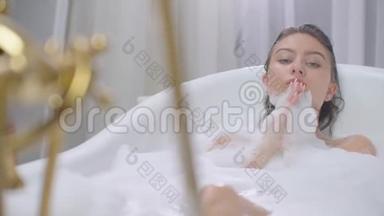 美丽的女人躺在浴缸里泡<strong>澡</strong>放松。 在有泡沫泡浴的浴缸里轻松愉快地躺着