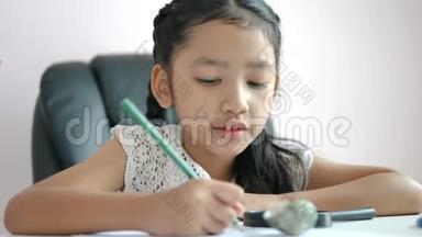 小亚洲女孩用铅笔在纸上写作业，微笑着为教育理念选择焦点