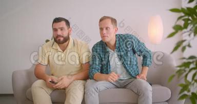 两名白人男子在电视上观看体育节目，并在家里一起坐在沙发上庆祝