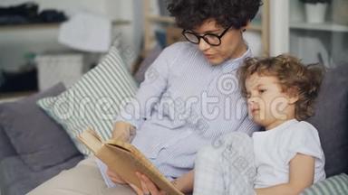 爱看书的妈妈给坐在房间沙发上的可爱的卷发男孩看书