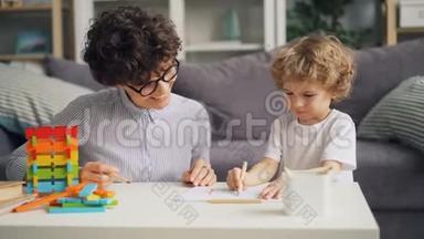 小男孩用铅笔画画，而开朗的女人在说话，微笑