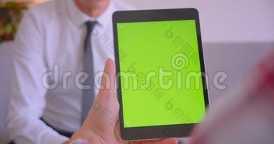 客户经理与客户手持平板电脑的特写肖像，办公室里有绿色的彩色键盘屏幕